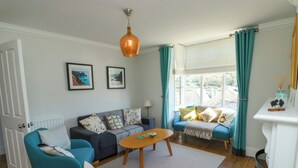 Een woonkamer met een bank, twee fauteuils, een salontafel, een open haard en een raam met gordijnen.