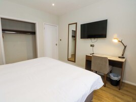 Una habitación de hotel con cama, escritorio, silla, televisor y lámpara de escritorio.