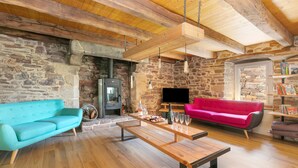 A cozy living room with a stone wall, wooden beams, a fireplace, a TV, and two sofas.