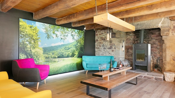 A modern interior with a stone fireplace, wooden ceiling beams, and a large window overlooking a scenic landscape.