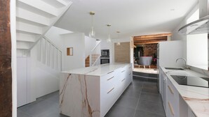 A modern kitchen with a marble island, white cabinetry, and a built-in stove.