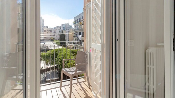 Un balcone con una sedia e vista sulla città, oltre a una porta bianca.