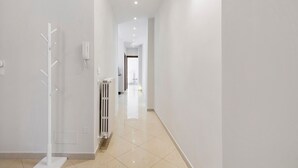 Un corridoio con un termosifone, un dispositivo bianco a parete e una porta in fondo.