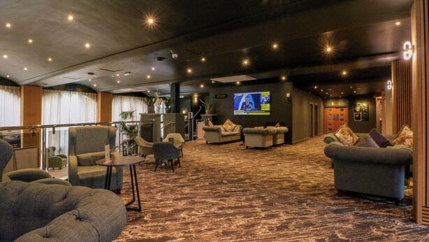 A hotel lobby with seating areas, a television screen, and a staircase. - Stag Lodge (Chorley)