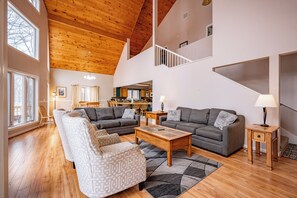 A spacious living area with a high ceiling, wooden flooring, and a modern kitchen in the background.