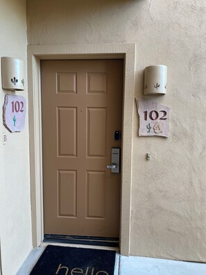 A brown door with a keypad lock, a doormat with 'hello' written on it, and two wall-mounted light fixtures with numbers '102' and a cactus symbol. - Cute 1 Bed  in the heart of Fountain Hills (Fountain Hills)