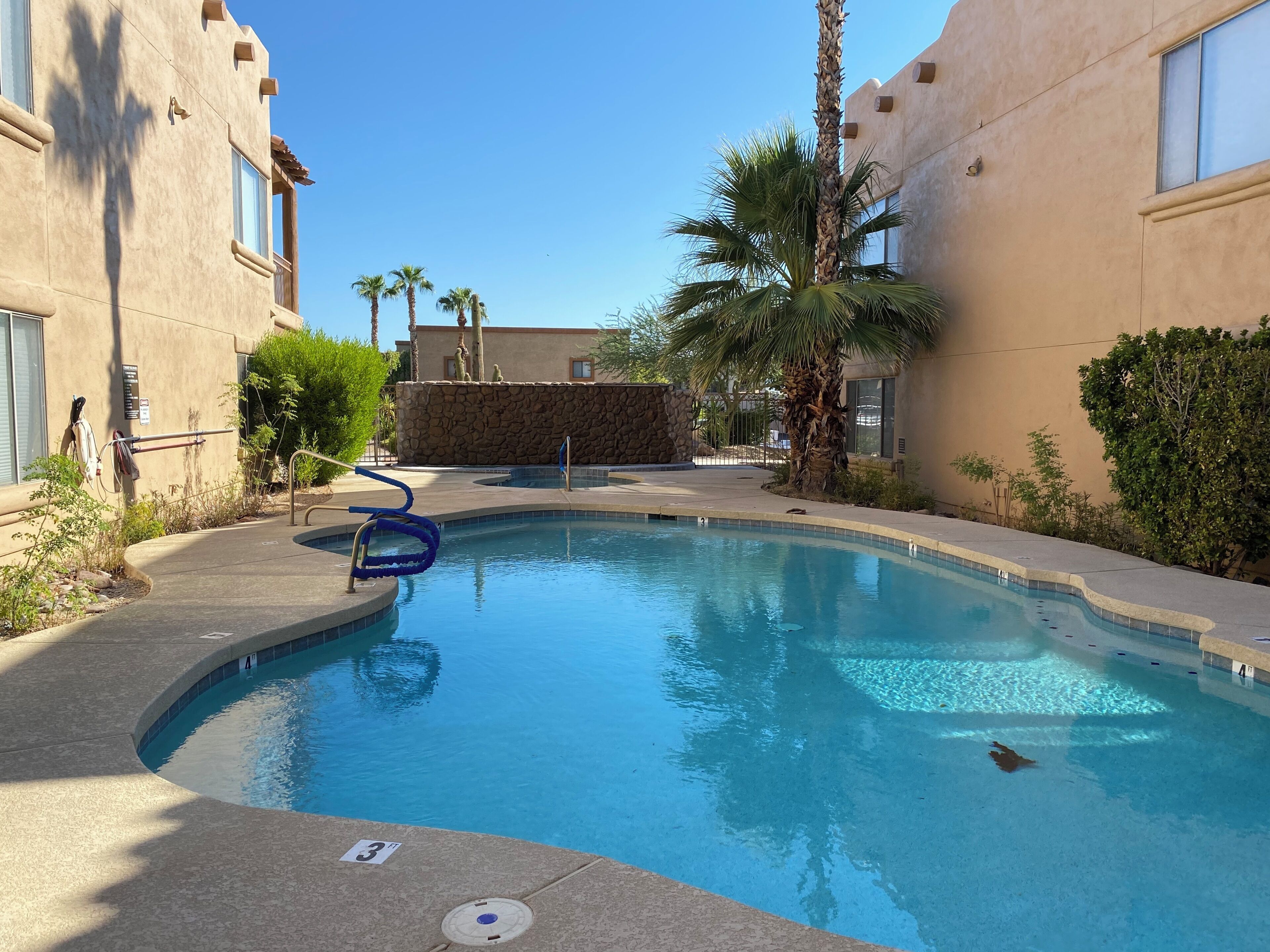 A swimming pool with a stone wall, palm trees, and a building with a stone facade.