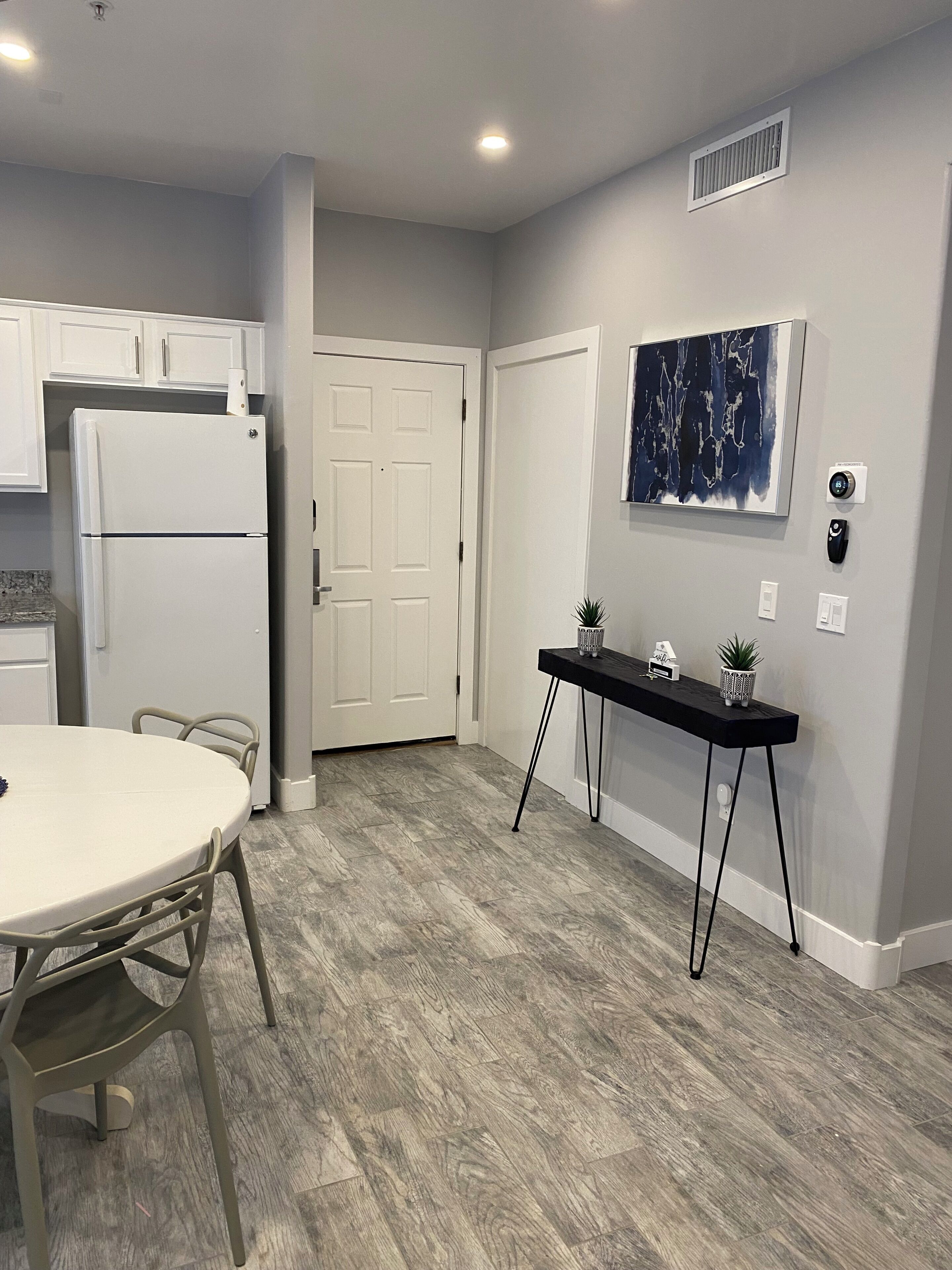 Una cocina moderna con un refrigerador blanco, una mesa de comedor con sillas y una consola negra con plantas.