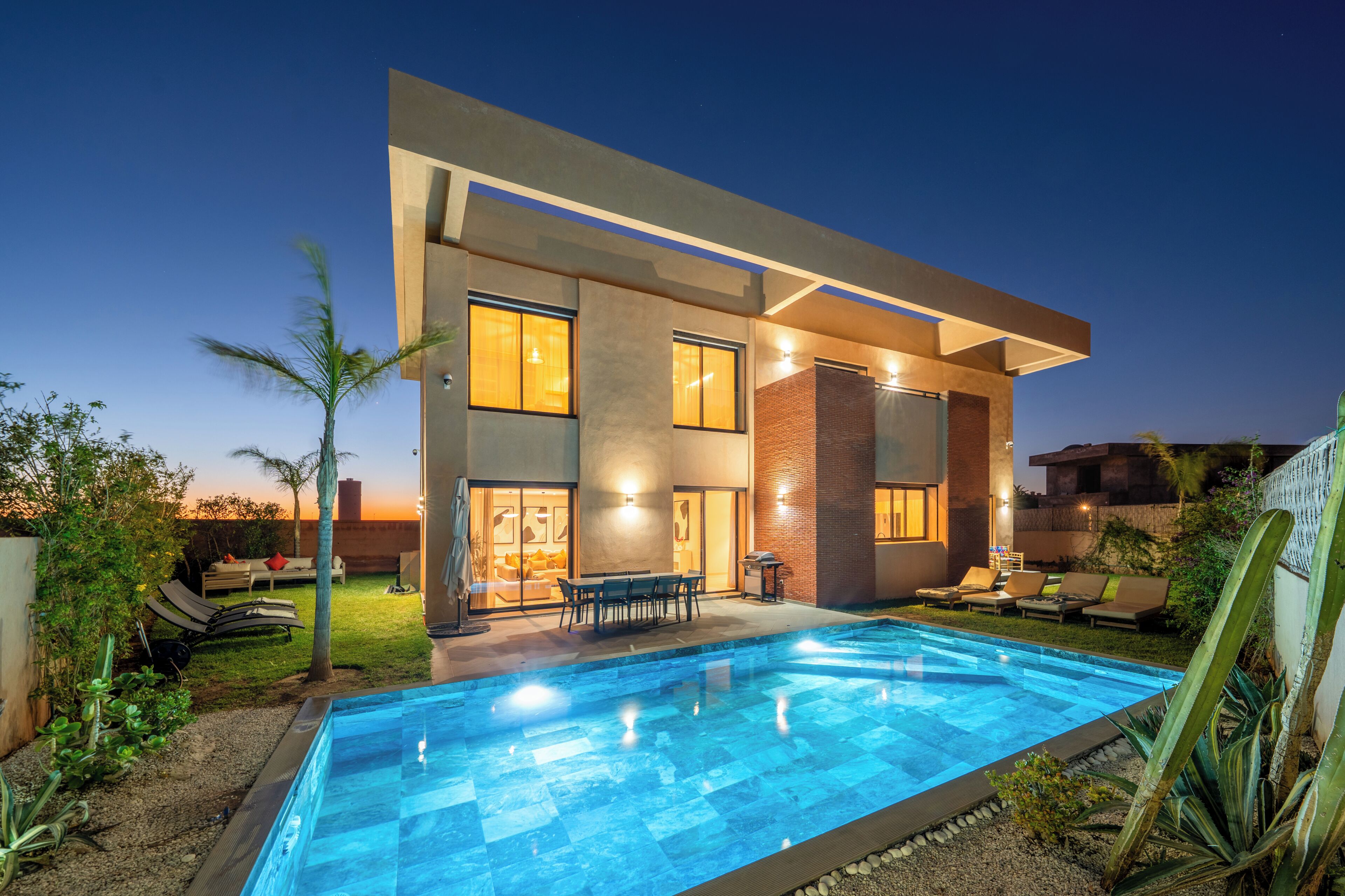A modern two-story house with a swimming pool, outdoor seating, and a well-lit patio area.