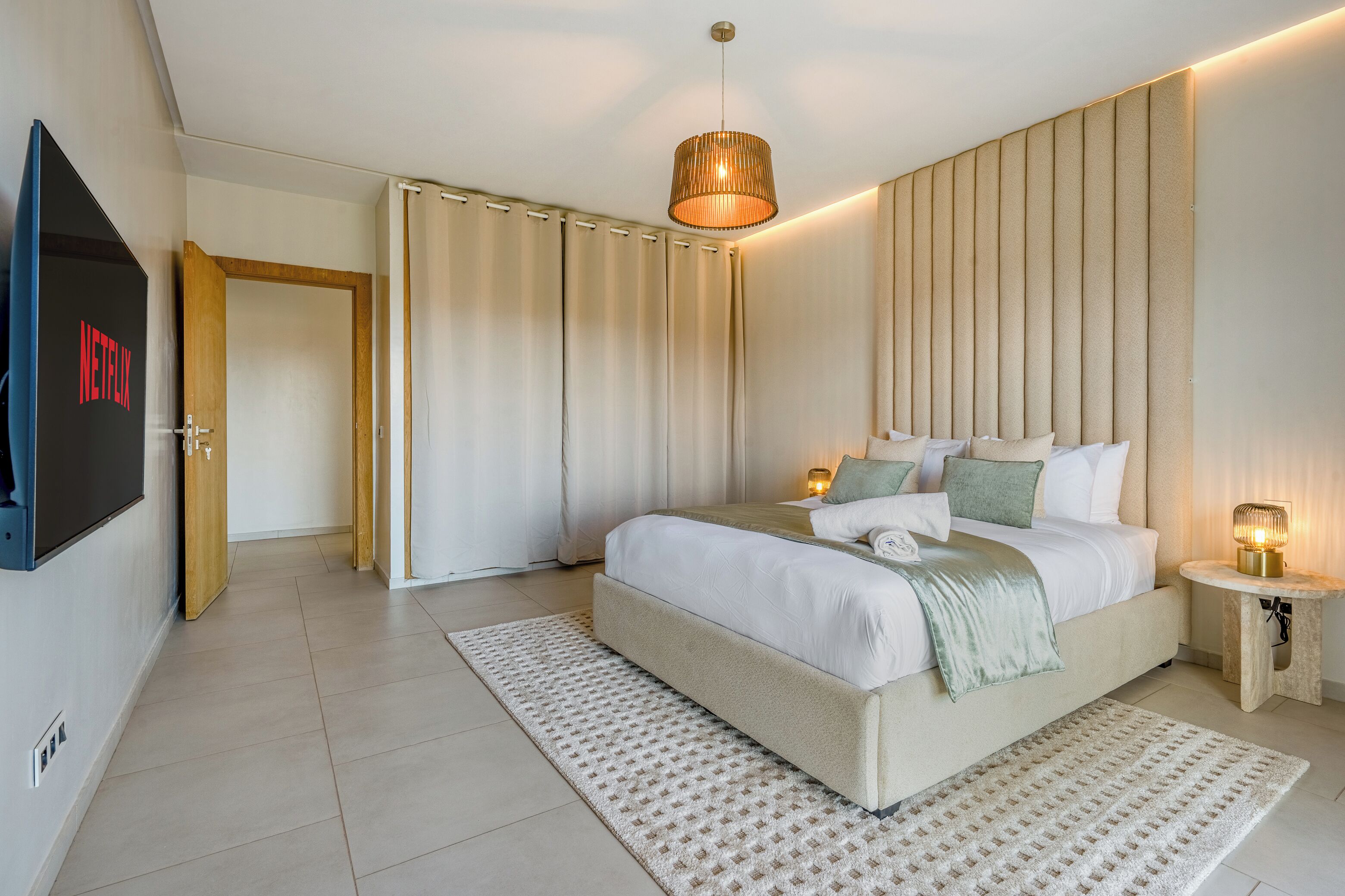 Quarto moderno com uma cama grande, uma TV na parede e uma mesa de cabeceira com abajur.