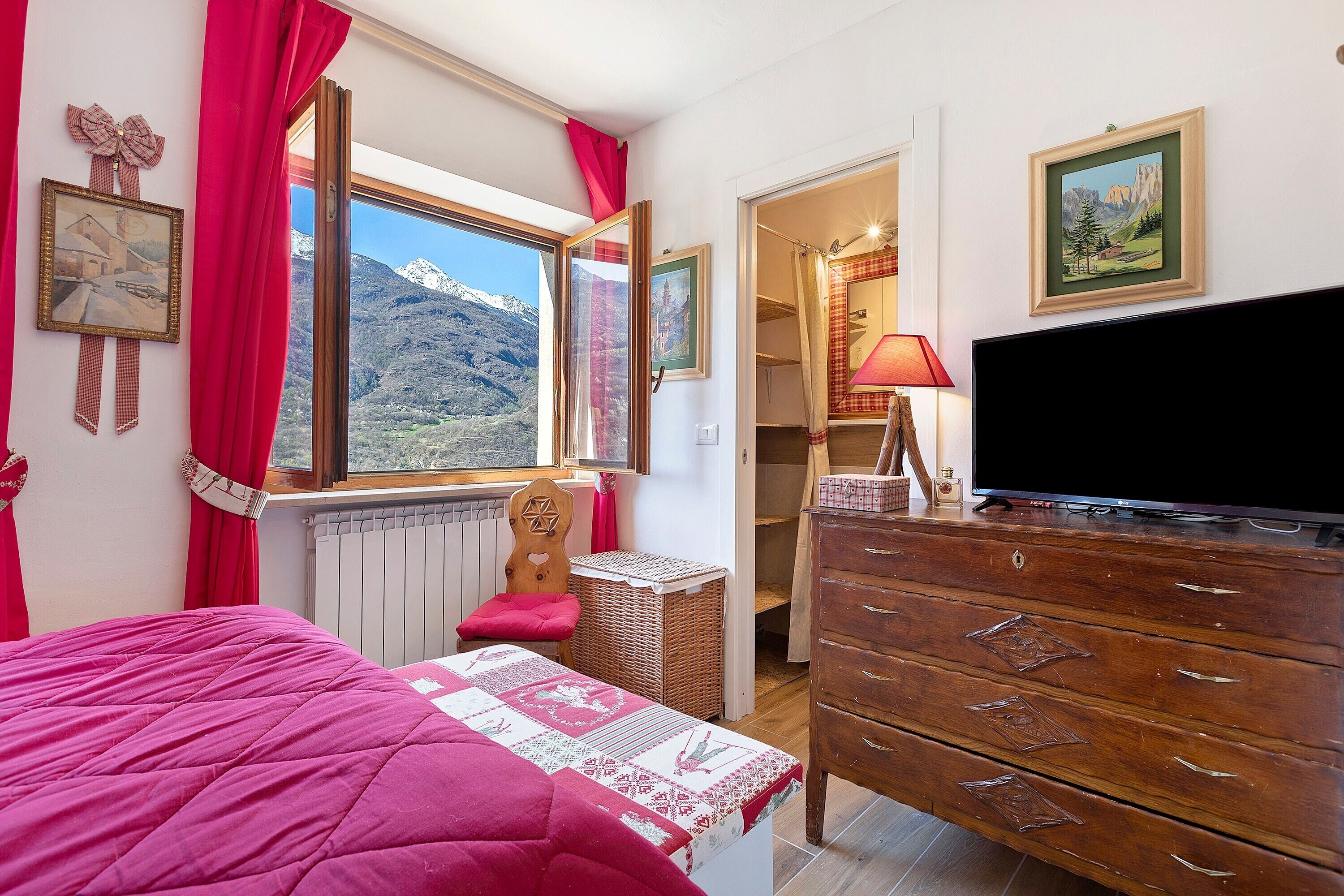 Une chambre à coucher comprenant un lit, une commode, une télévision et une fenêtre donnant sur les montagnes.