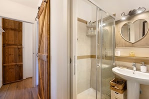 A modern bathroom with a glass shower enclosure, wooden door, and a heart-shaped mirror.