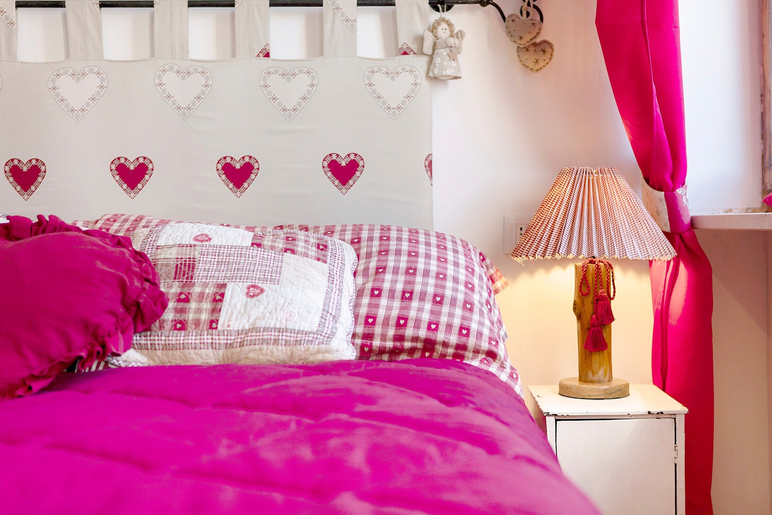 A bed with pink bedding, a bedside lamp, and heart-themed decor on the wall.