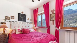 A bedroom with a large bed, a window with curtains, a radiator, and wall decorations. - Bellavista Saint-Vincent (Saint-Vincent)