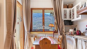 A dining area with a view of mountains, a wooden table, chairs, and a kitchen with cabinets and appliances. - Bellavista Saint-Vincent (Saint-Vincent)