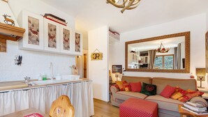 A cozy living room with a sofa, a wooden coffee table, a kitchen area with a sink and cabinets, and a large mirror on the wall. - Bellavista Saint-Vincent (Saint-Vincent)