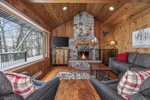 L’intérieur d’un chalet chaleureux, avec une cheminée en pierre, des murs en bois, un canapé et un téléviseur.
