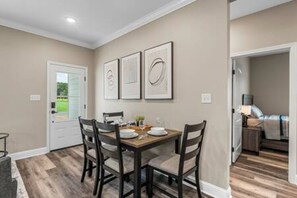 Un coin repas avec une table dressée pour quatre personnes, une porte sur la gauche et un couloir menant à une chambre.