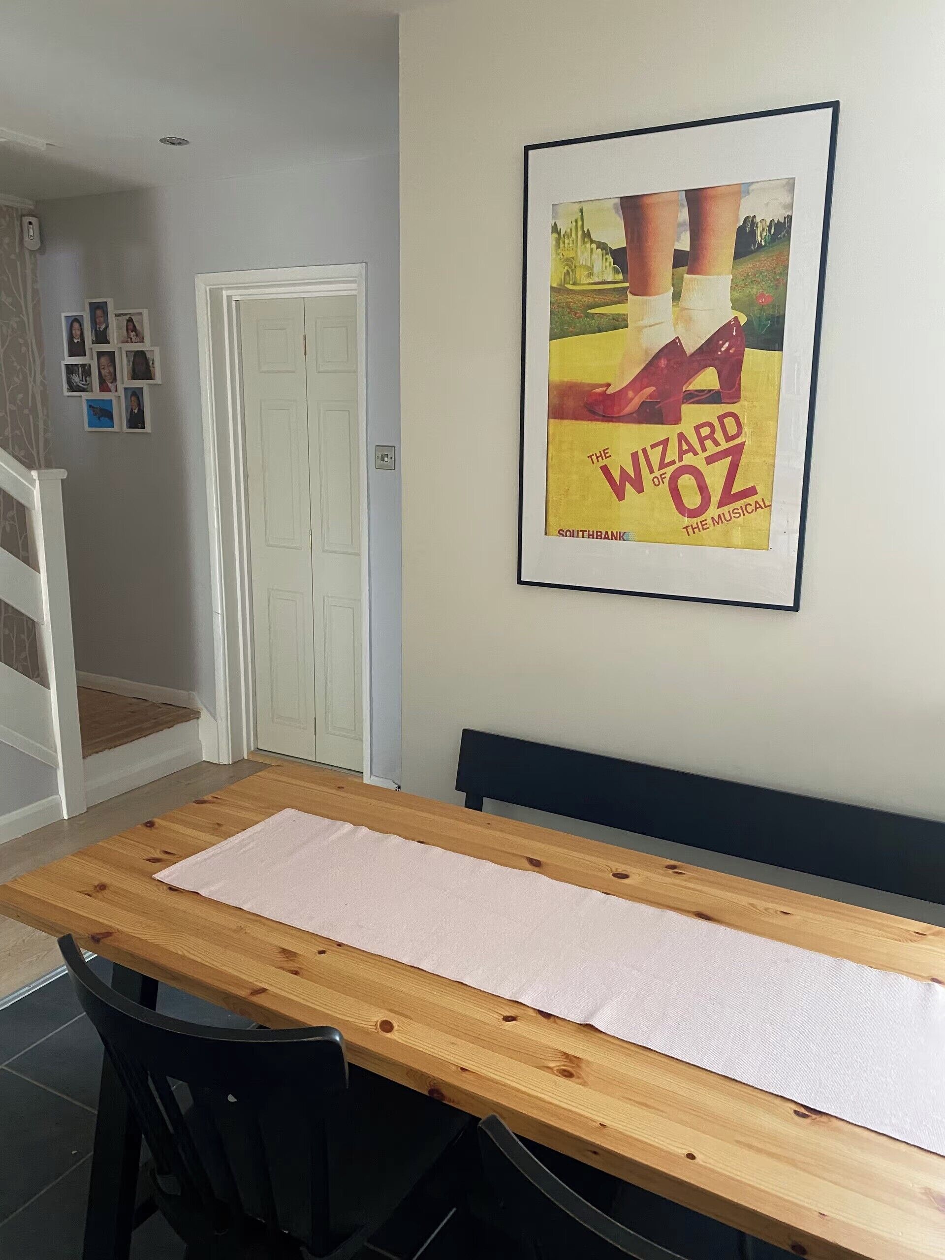 A dining area with a wooden table, black chairs, a framed poster of 'The Wizard of Oz,' and a white door.