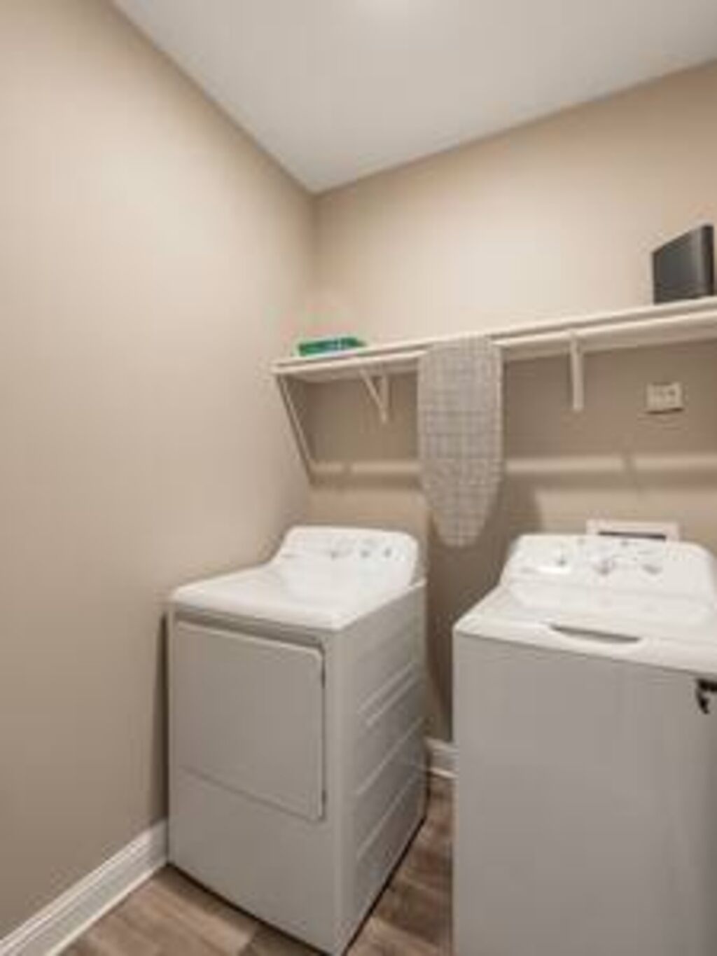 A laundry room with two white washing machines, a shelf with a green box, and a tiled floor.