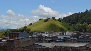 A hilly landscape with a small building on top, surrounded by residential buildings.