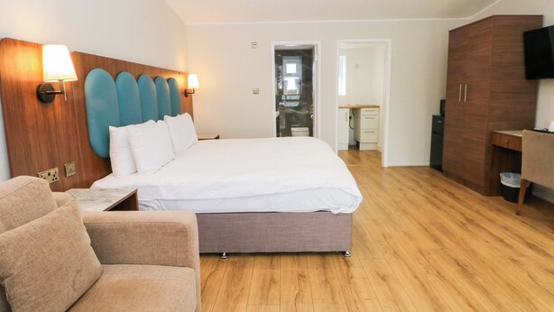 Una habitación de hotel moderna con una cama grande, cabecera de madera, zona de estar con sofá, armario de madera y televisor.