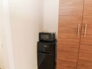 Eine kleine Küche mit Mikrowelle und Kühlschrank, Holzschränken und einer weißen Wand.