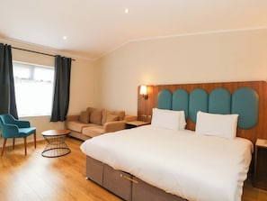 A hotel room with a large bed, a sofa, a chair, a small table, and a window with curtains. - Fox Lodge (Chorley)