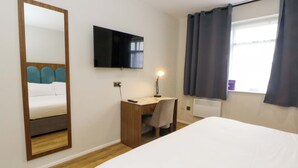 Habitación de hotel con cama, escritorio, silla, televisor, ventana con cortinas y espejo.