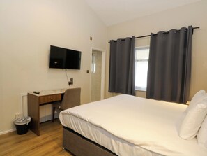 Une chambre à coucher avec un lit, un bureau, une chaise, une télévision et une fenêtre avec des rideaux.