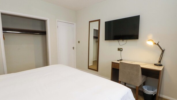 Una habitación de hotel con cama, un escritorio con silla, televisión y una lámpara de escritorio.