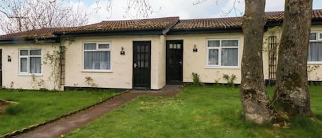 A two-story house with a tiled roof, a front door, and a small front yard with grass and a pathway.
