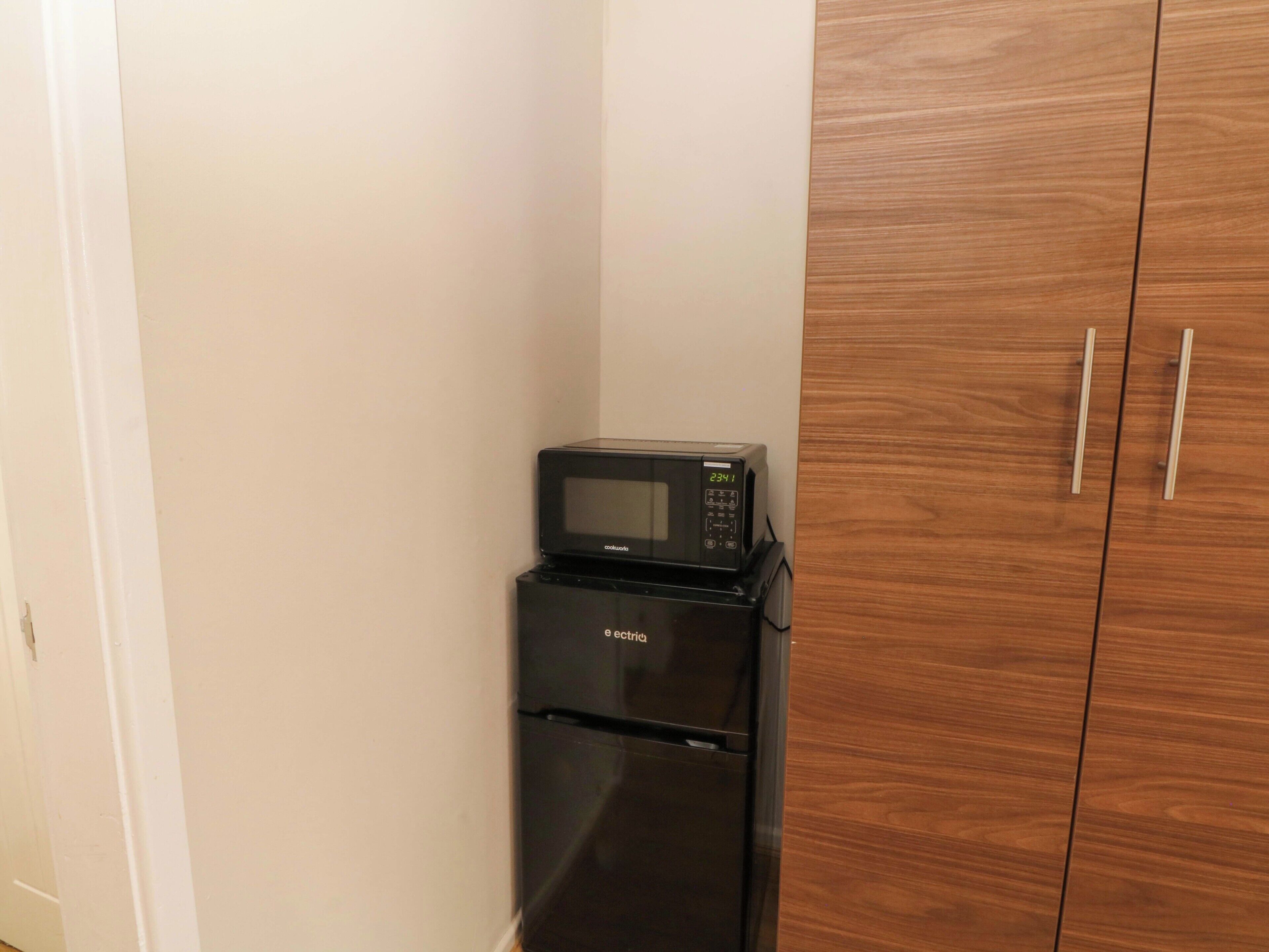 A compact kitchen with a black refrigerator and microwave, wooden cabinets, and a white wall.
