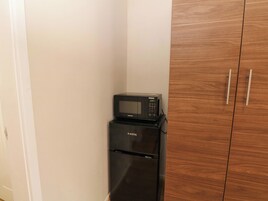 A compact kitchen with a black refrigerator and microwave, wooden cabinets, and a white wall.