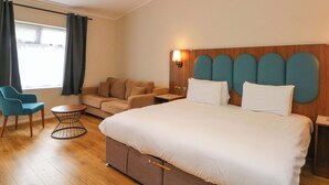 Ein Hotelzimmer mit Bett, Sofa, Sessel, kleinem Tisch und einem Fenster mit Vorhängen.