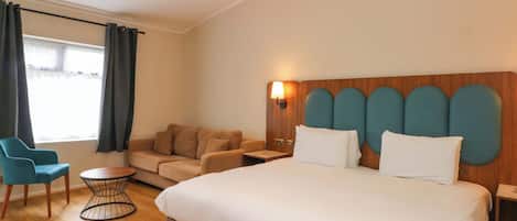 A hotel room with a bed, a sofa, a chair, a small table, and a window with curtains.