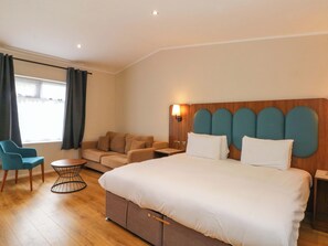 A hotel room with a bed, a sofa, a chair, a small table, and a window with curtains. - Deer Lodge (Chorley)