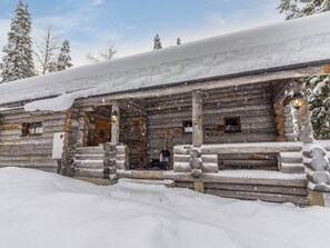 A log cabin with a snow-covered roof, wooden walls, and a stone foundation.