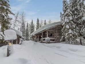 Une cabane en rondins avec un porche, entourée d’arbres couverts de neige.