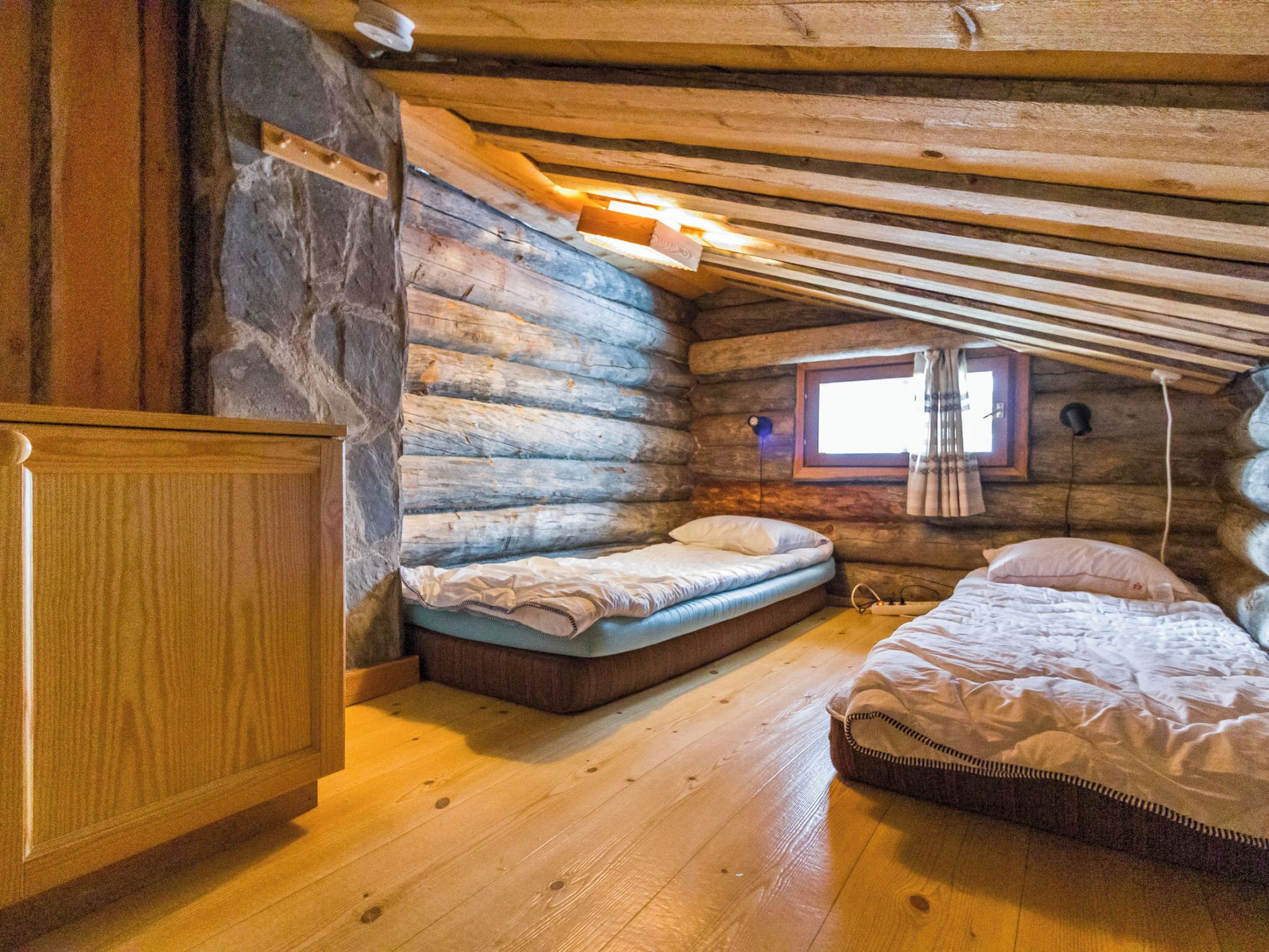 A log cabin bedroom with a wooden floor, a stone wall, a window, and a bed.