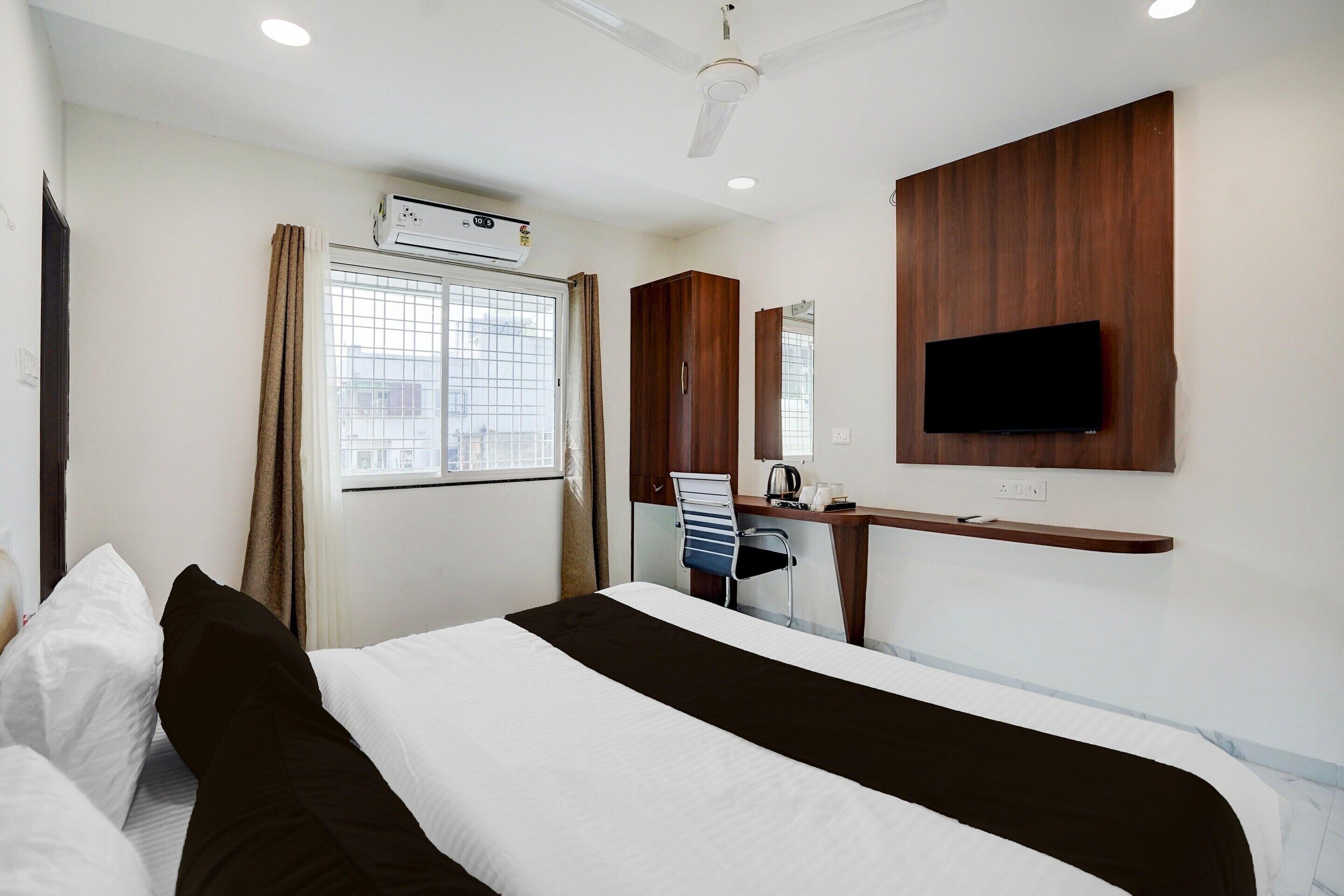 A hotel room with a bed, desk, chair, television, and an air conditioning unit.