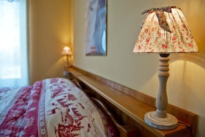 A bed with a floral-patterned bedspread, a wooden bedside table with a lamp, and a poster on the wall. - 'Room 1' with Mountain View, Shared Terrace in Bionaz (Dzovennoz)