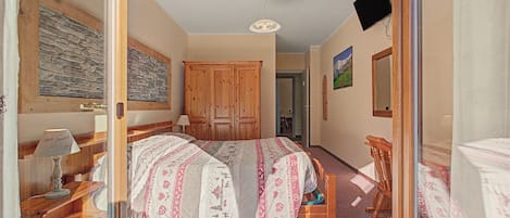 A bedroom with a bed, wooden wardrobe, and a mirror.