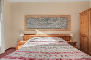 A bedroom with a bed, wooden headboard, two bedside tables, a nightstand, a wardrobe, and a stone wall decoration. - 'Room 1' with Mountain View, Shared Terrace in Bionaz (Dzovennoz)