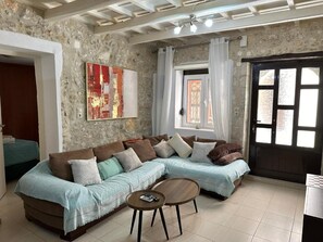 A living room with a sectional sofa, a coffee table, a painting on the wall, and a window with curtains. - Casa Joanna Old town Rethymno (Rethimno)