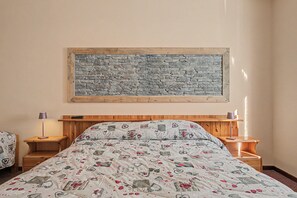 A bedroom with a bed, two nightstands, a wall-mounted painting, and a patterned bedspread. - 'Triple Room 3' with Shared Terrace in Bionaz (Dzovennoz)