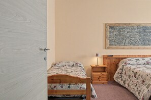 A bedroom with two beds, a wooden headboard, a nightstand, a lamp, and a wall-mounted artwork. - 'Triple Room 3' with Shared Terrace in Bionaz (Dzovennoz)