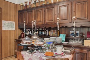 A bar area with wooden cabinets, a variety of bottles, and a buffet table with food and drink items. - 'Triple Room 3' with Shared Terrace in Bionaz (Dzovennoz)