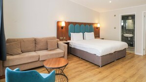 A hotel room with a bed, a sofa, a small round table, and a bathroom with a sink. - Otter Lodge (Chorley)