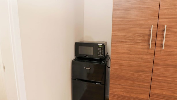 A compact kitchen with a microwave and refrigerator, wooden cabinets, and a white wall. - Otter Lodge (Chorley)